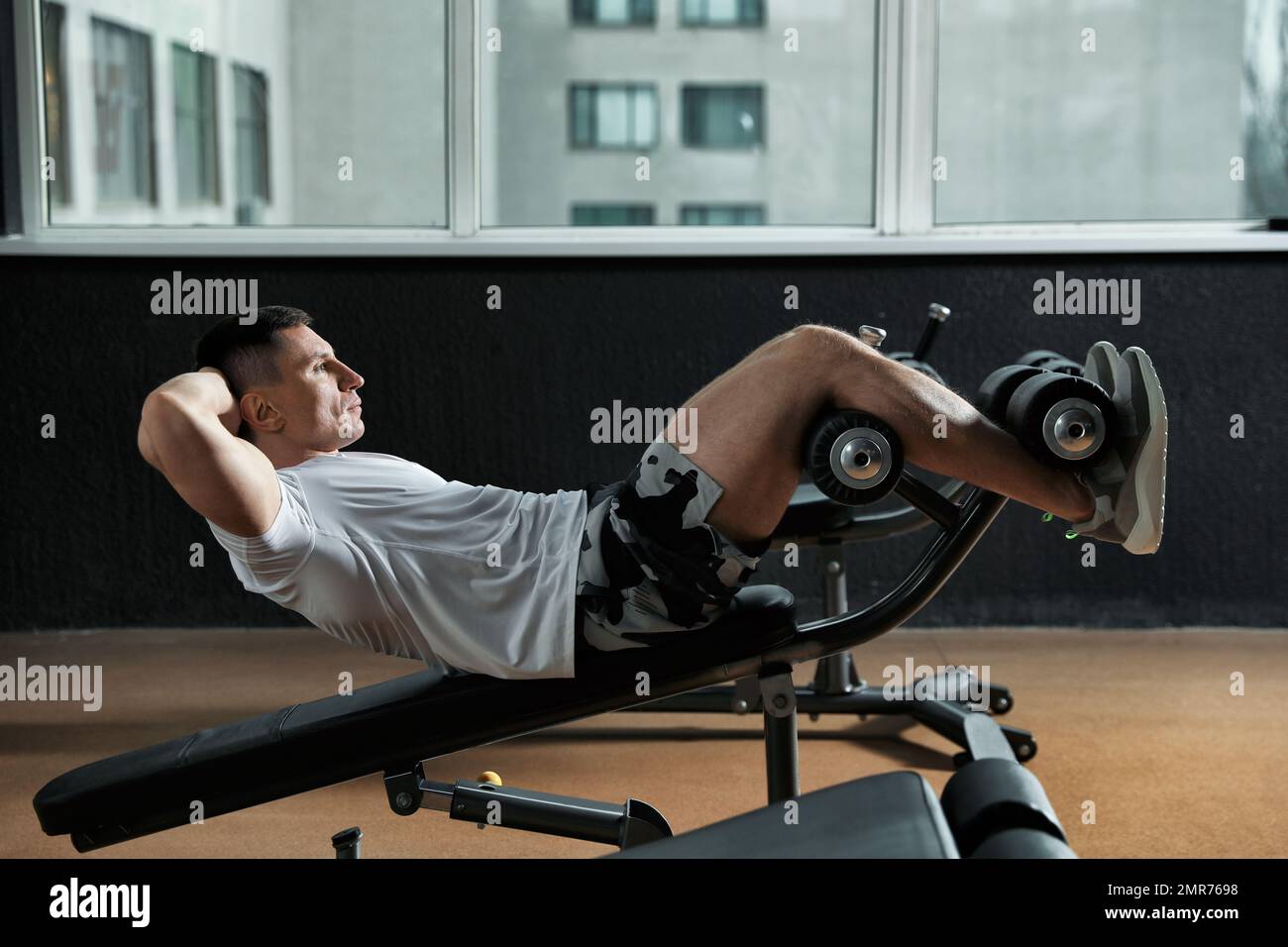 Man working out on adjustable sit up bench in modern gym Stock