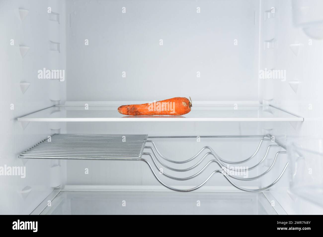 Old carrot on empty shelf in refrigerator Stock Photo