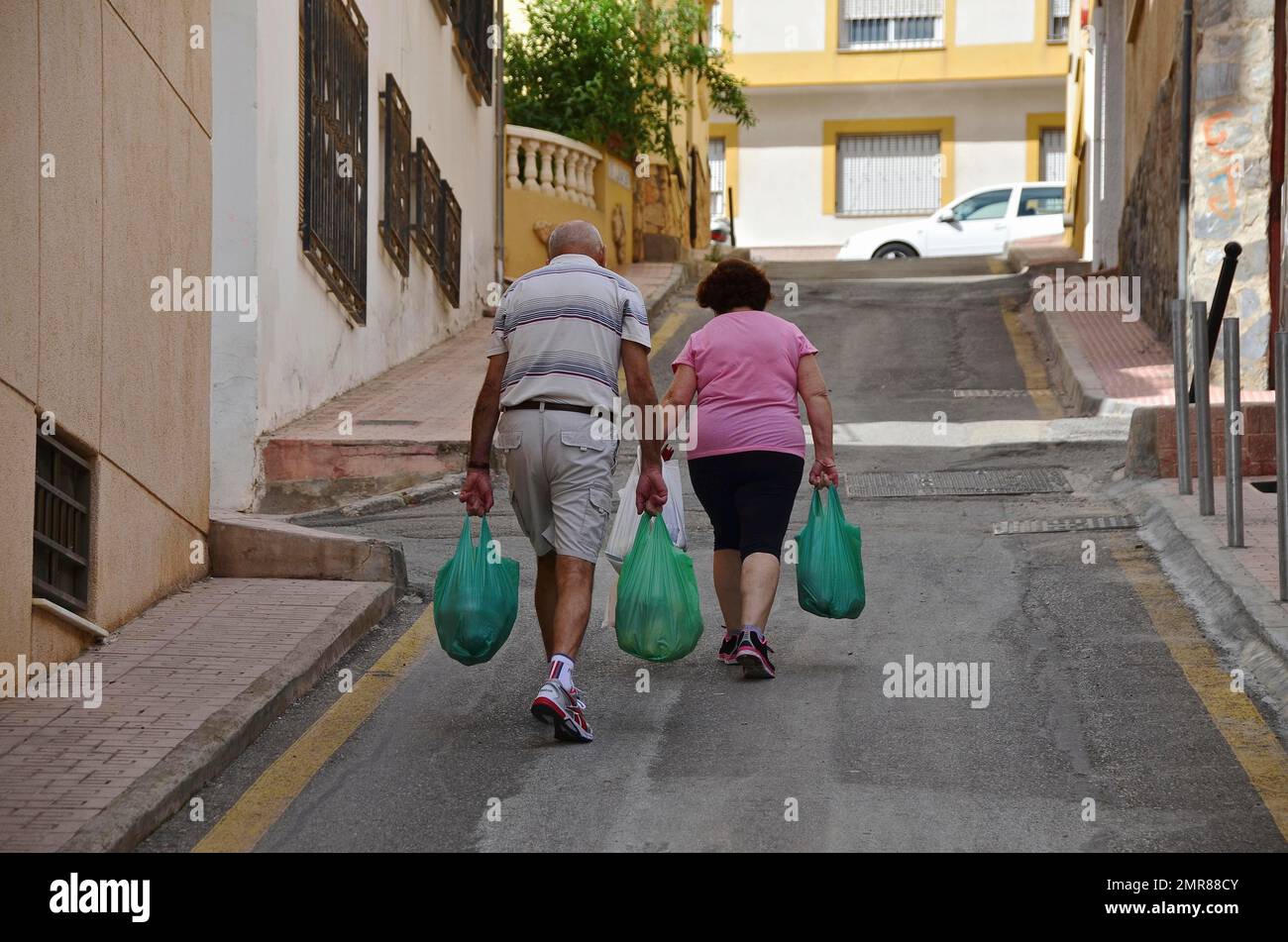 Couple from behind walking up steep street with green shopping bags, Garrucha, Andalucia, Spain, Europe Stock Photo