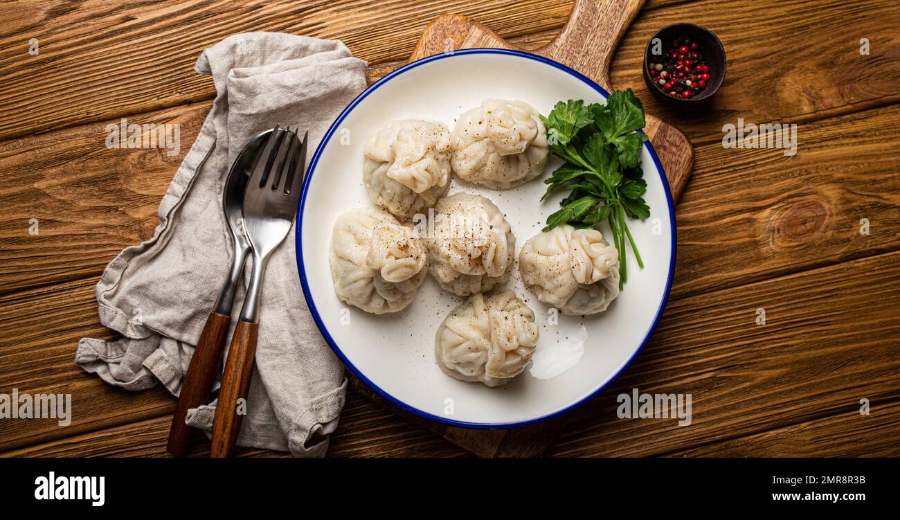 Khinkali, traditional dish of Georgian Caucasian cuisine, dumplings filled with ground meat on white plate with herbs on wooden rustic background tabl Stock Photo