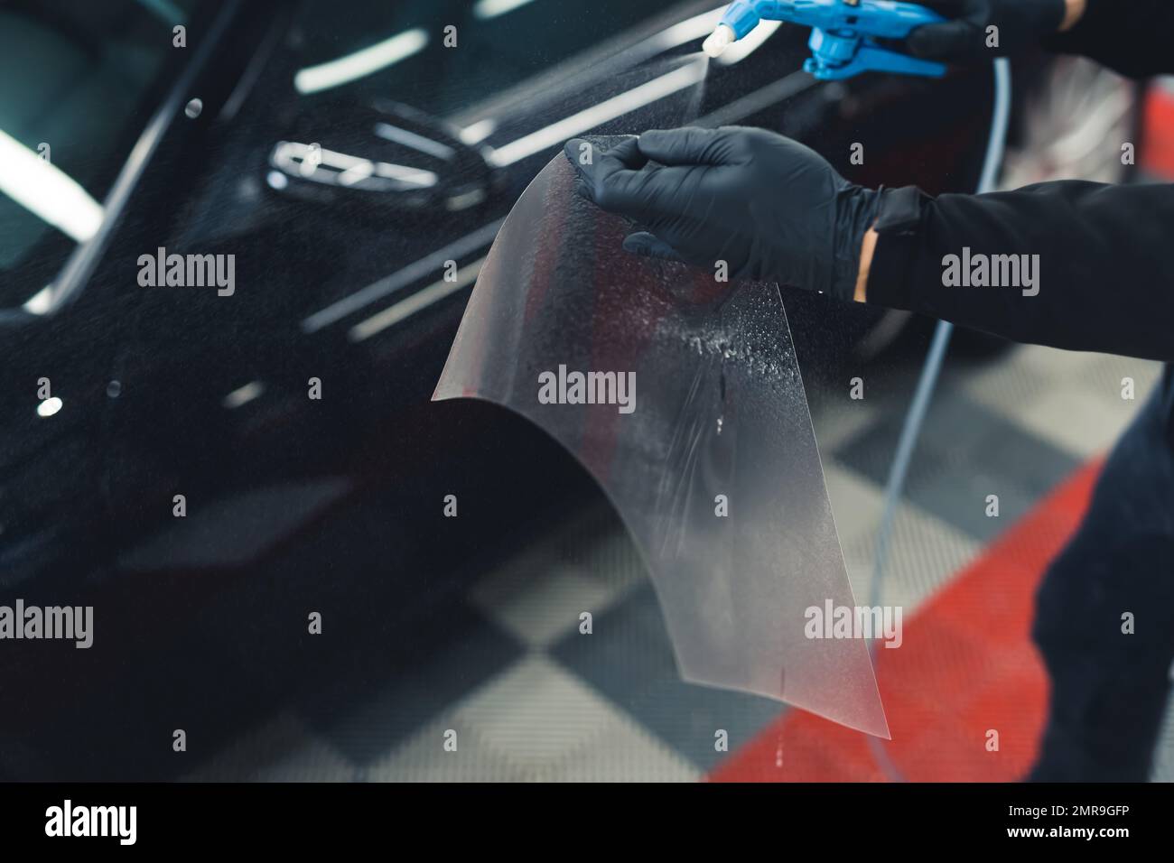 Paint protection film installation on side mirror of a black sports car