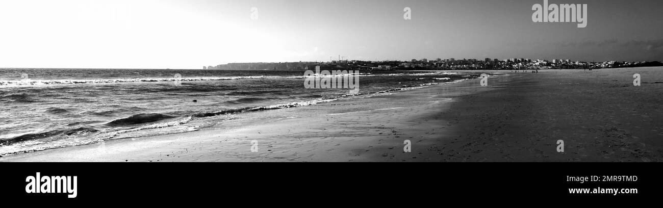 A panoramic view of a sandy beach and a distant city skyline. Black-and-white photography. Stock Photo