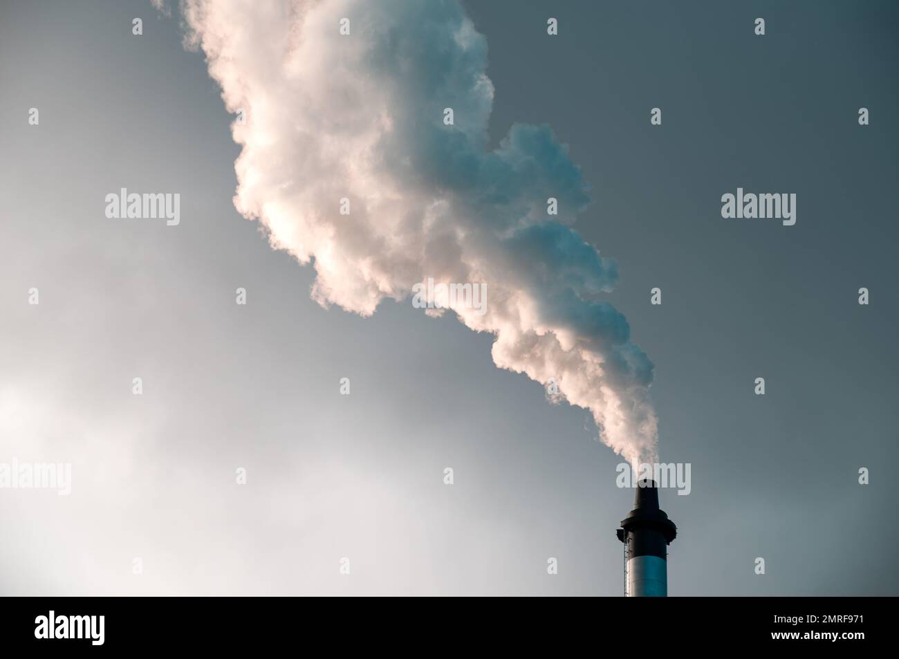 The white smoke coming out of the chimney against the gray daytime sky cloudy sky Stock Photo