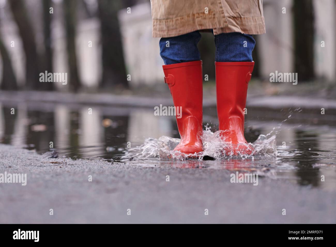 Woman in rubber boots jumping over puddle on rainy day, closeup. Space
