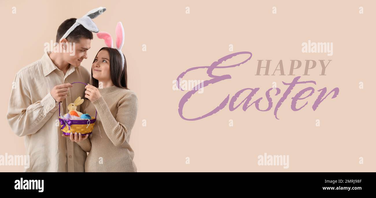 Banner with happy young couple in bunny ears and with Easter eggs in basket on beige background Stock Photo