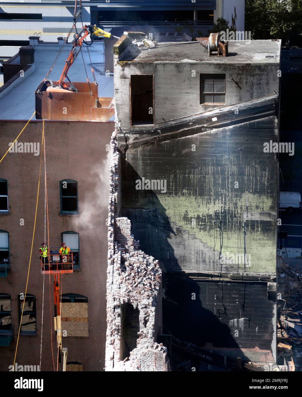 Workers use a remote control jackhammer, suspended by crane in a bucket