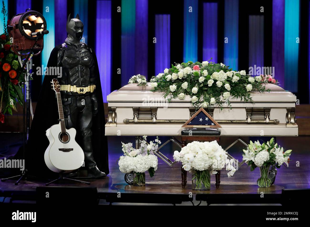 A Batman costume and guitar stand next to the casket during a memorial