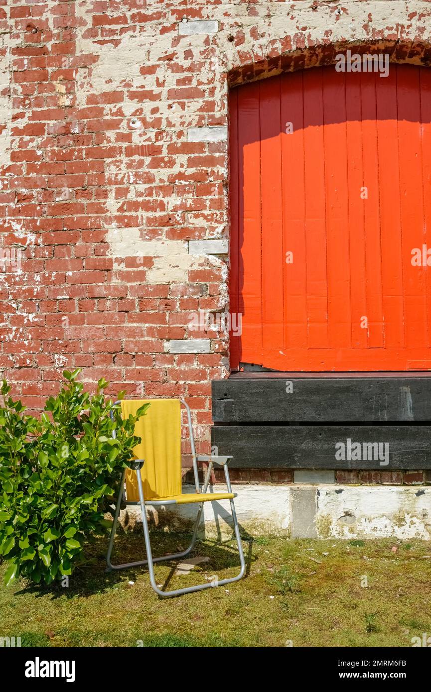 Red factory door in brick wall with empty yellow folding chair Stock Photo