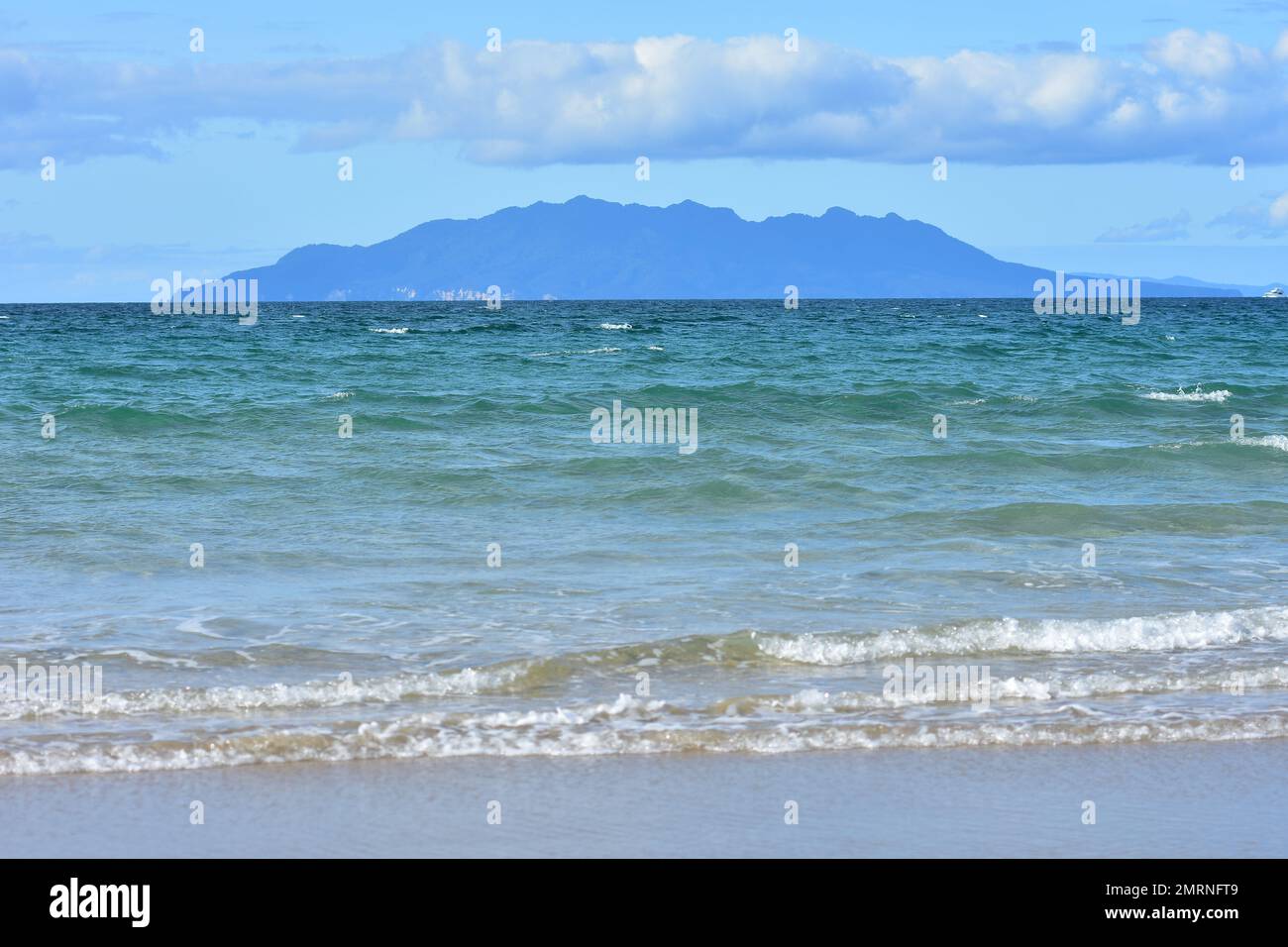 Little Barrier Island behind oceanic sandy beach with mild surf