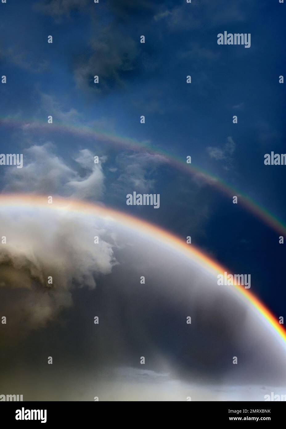 A bright double rainbow after rain against a blue sky and white clouds ...