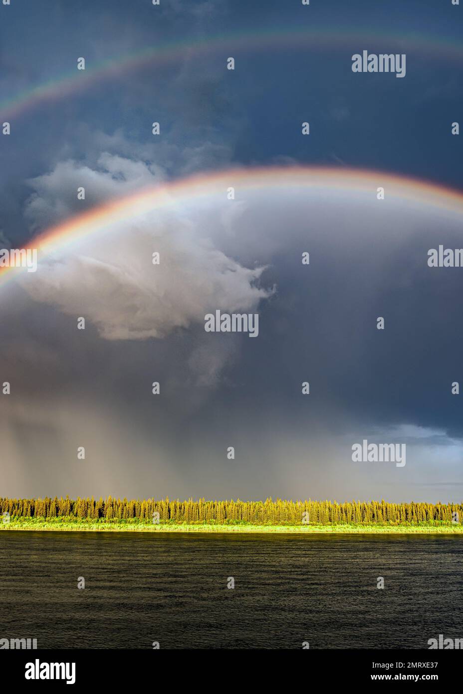 A bright double rainbow after rain during the day over a river against ...