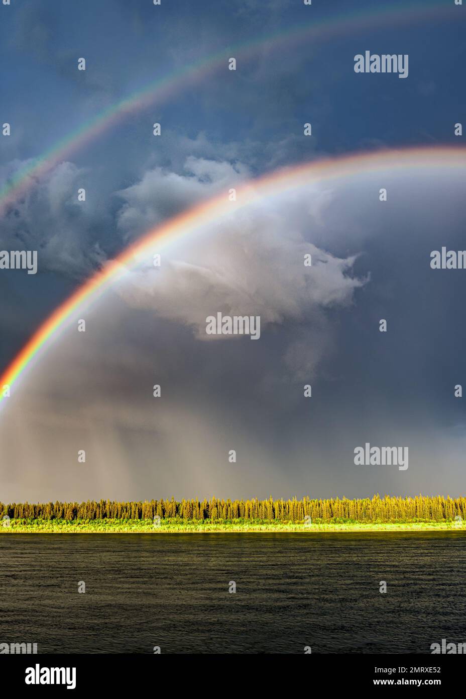 A bright double rainbow after rain during the day over a river against ...
