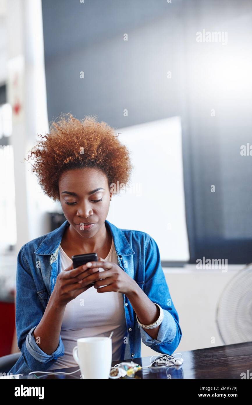 Catching up on text messages during her coffee break. a beautiful young woman using a mobile phone in a casual office. Stock Photo