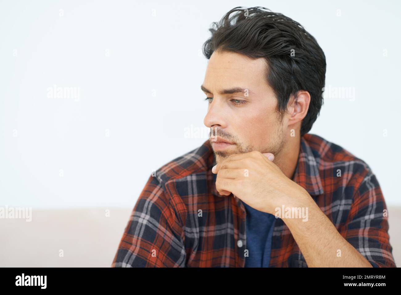 Lost in his thoughts. A gorgeous young man sitting on a sofa with hand ...