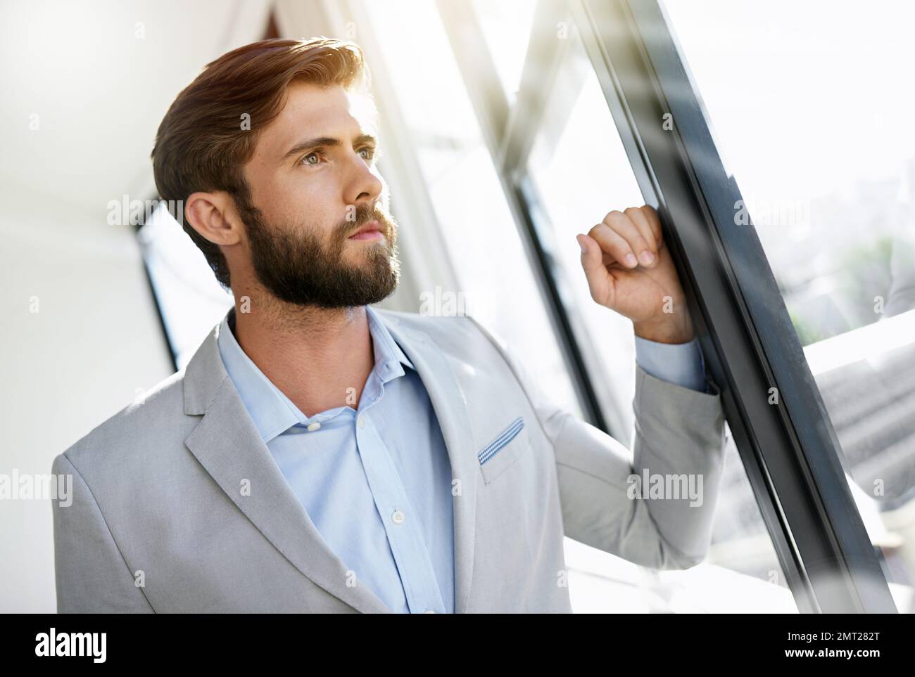 The vision of an ambitious man. an ambitious young businessman looking through his office window. Stock Photo