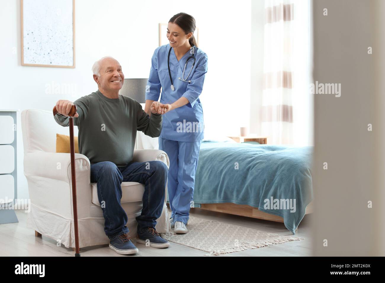Care worker helping elderly man with stick in geriatric hospice Stock Photo