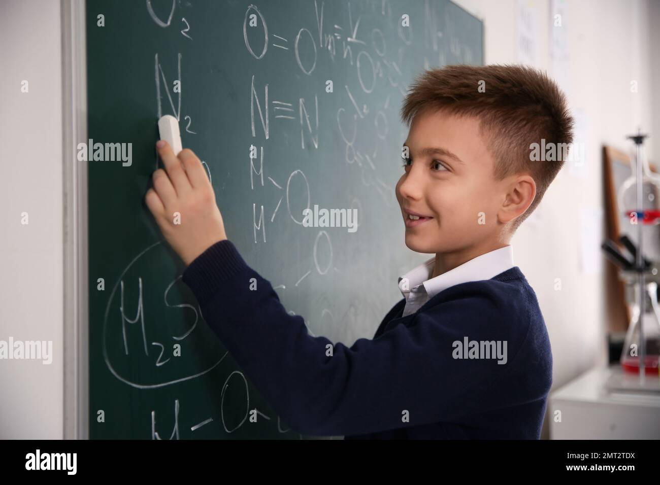 Schoolboy writing chemical formulas on chalkboard in classroom Stock