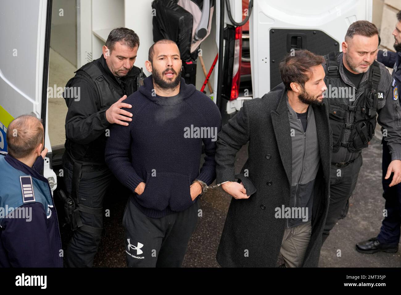 Police Officers Escort Andrew Tate, Center Left, Handcuffed To His ...