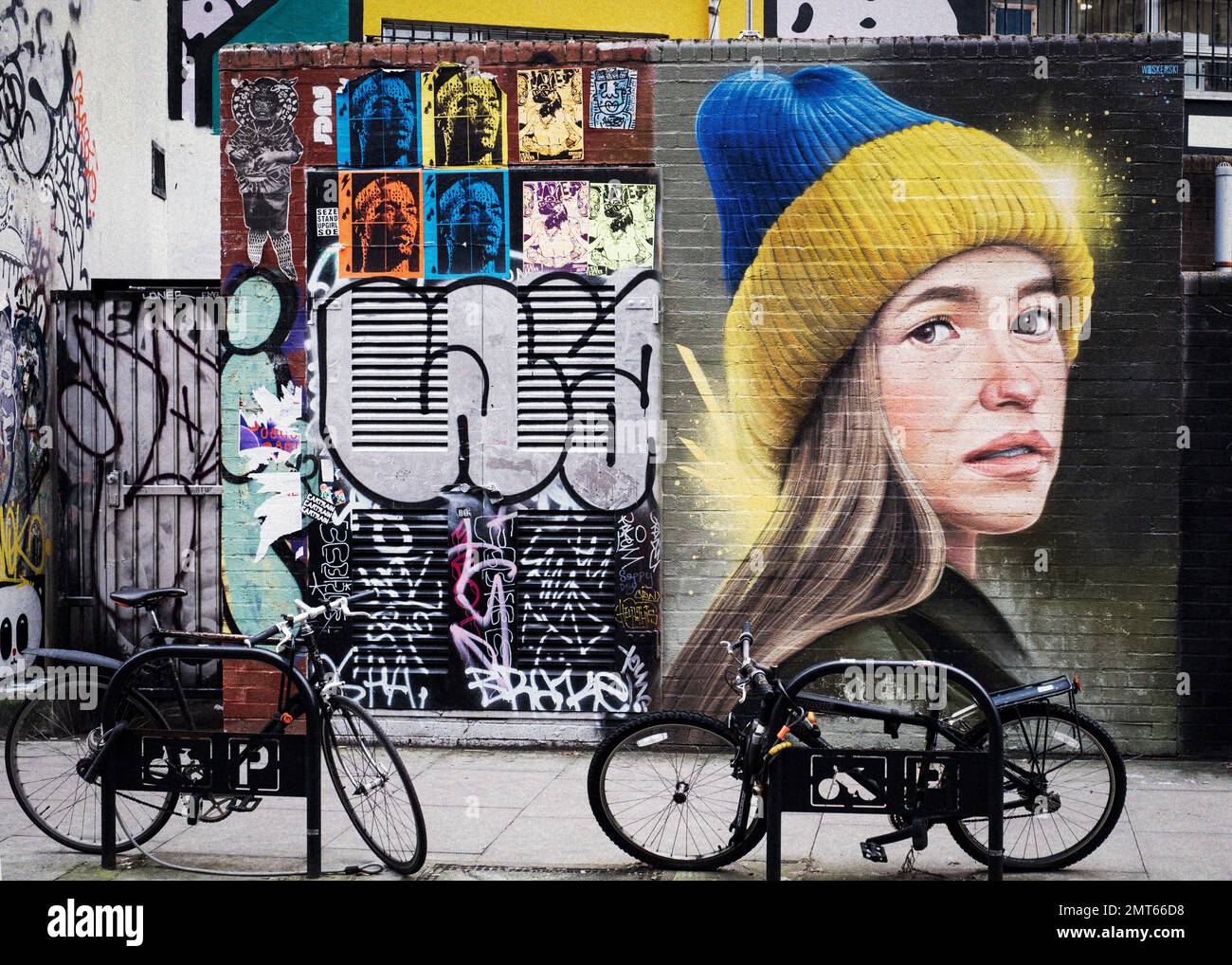 Artful graffiti portrait at Shoreditch East London with parked bicycles in foreground Stock Photo