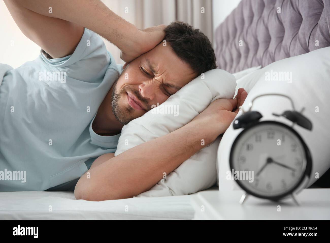 Sleepy man closing ears at home in morning Stock Photo