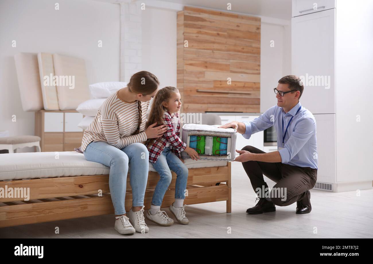 Salesman showing young woman and her daughter section of mattress in