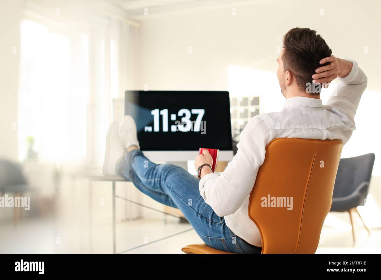 Young businessman with cup of drink relaxing at table in office during break Stock Photo