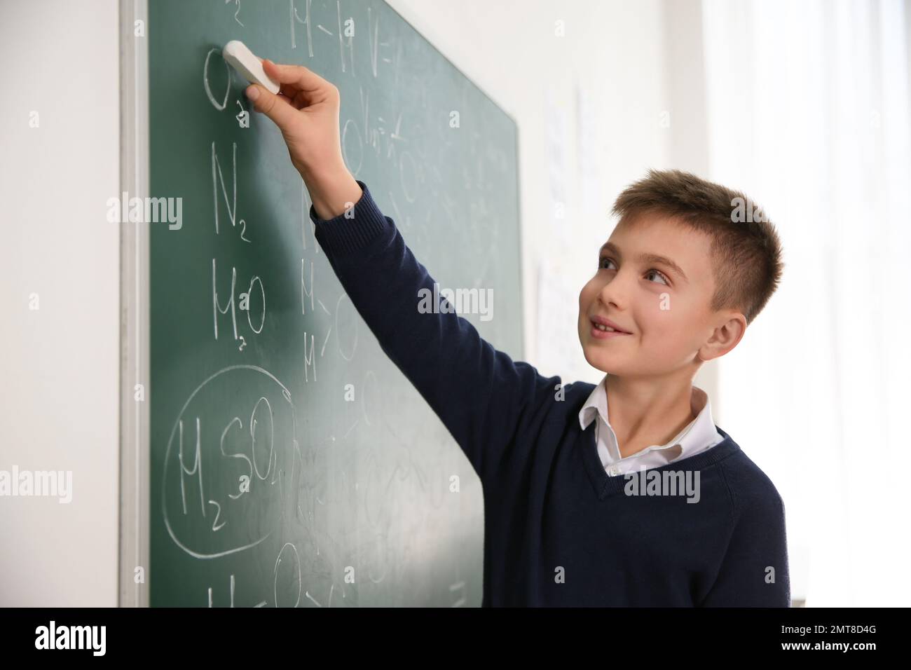 Schoolboy writing chemical formulas on chalkboard in classroom Stock