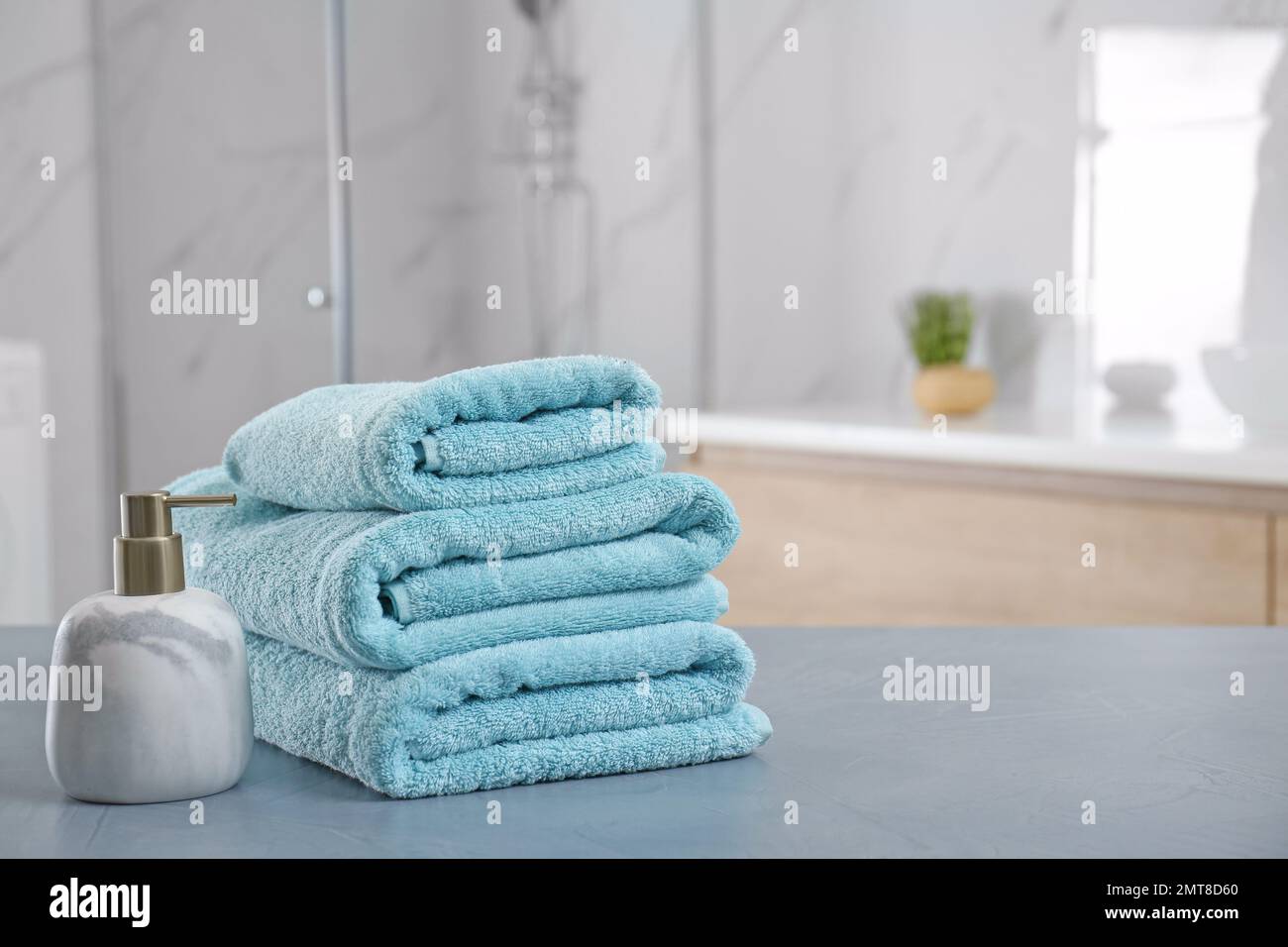 Stack of clean towels and soap dispenser on grey stone table in