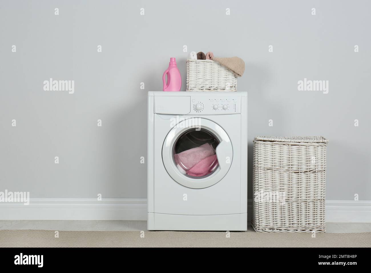 Modern washing machine with laundry, wicker baskets and detergent near ...