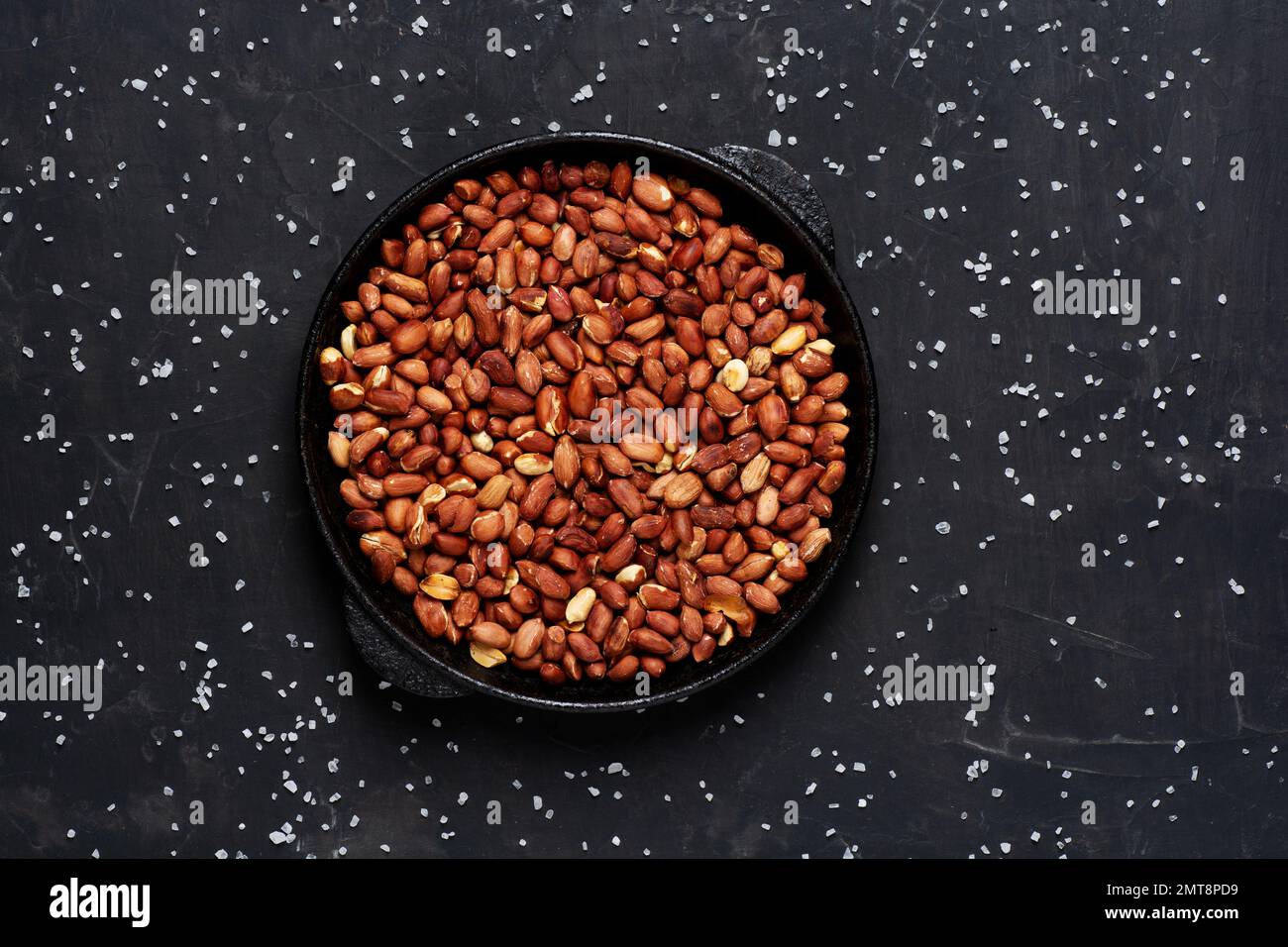 Roasted fresh peanuts in a frying pan on a black background with salt