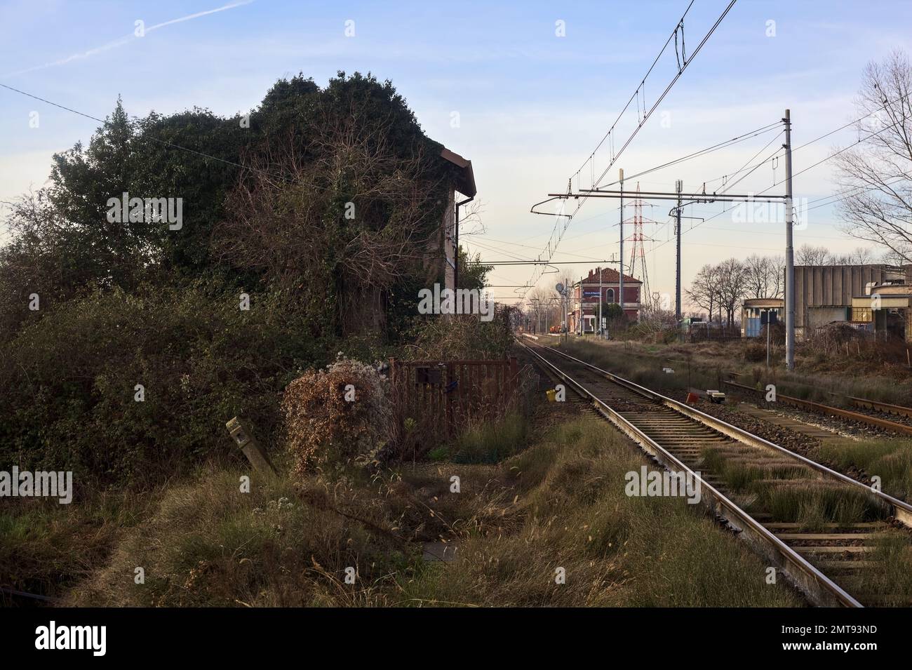 Abandoned  building covered by ivy by the edge of a railroad track on a cloudy day in the italian countryside Stock Photo