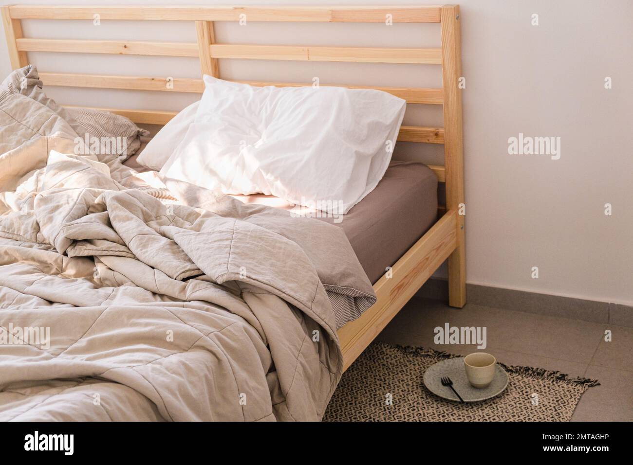 Morning wooden bed with beige linens after breakfast, copy space. Real life, mess concept. Stock Photo