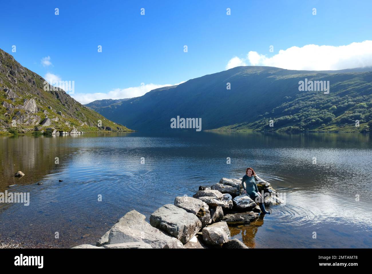 Attractive female tourist sitting on a rocky outcrop, Glenbeg Lake, County Cork, Ireland - John Gollop Stock Photo