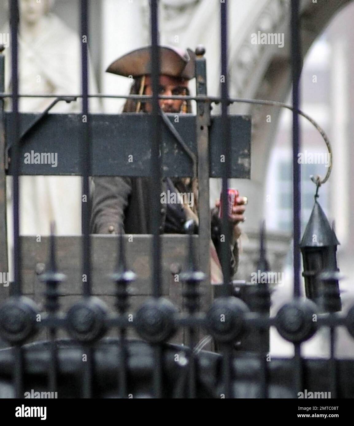 A stunt double dressed as Johnny Depp's character Captain Jack Sparrow sips on a soda and later is filmed driving a burning carriage on the set of 'Pirates of the Caribbean: On Stranger Tides' filming at Greenwich's Old Royal Naval College while excited fans tried to catch a glimpse of the action by climbing a fence. London, UK. 10/09/10. Stock Photo