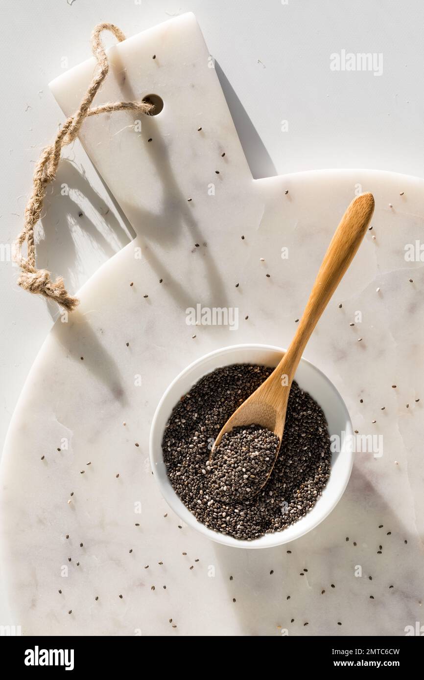 A bowl of chia seeds on a white marble board in bright sunlight. Stock Photo