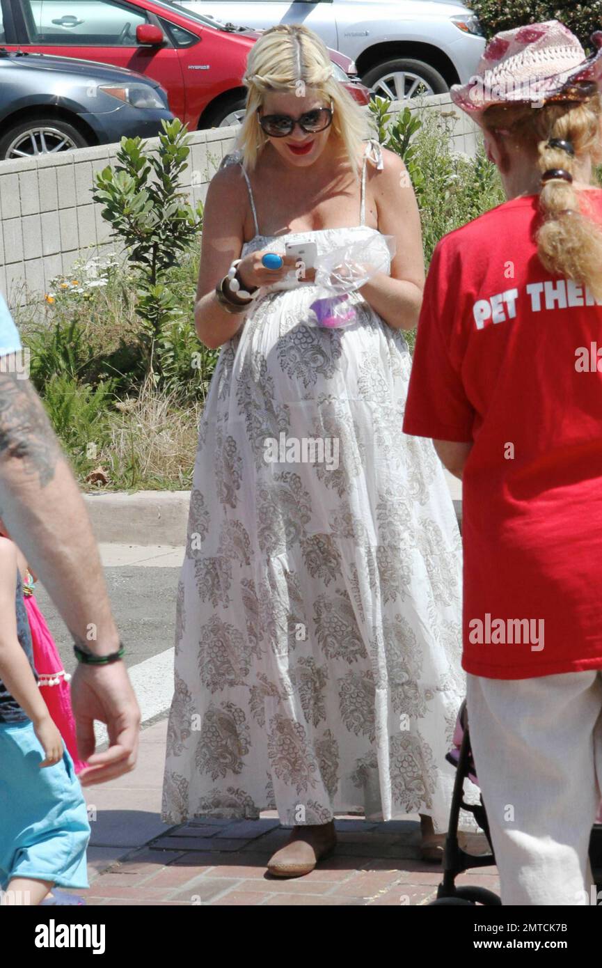 A heavily pregnant Tori Spelling in a long lose fitting white dress and