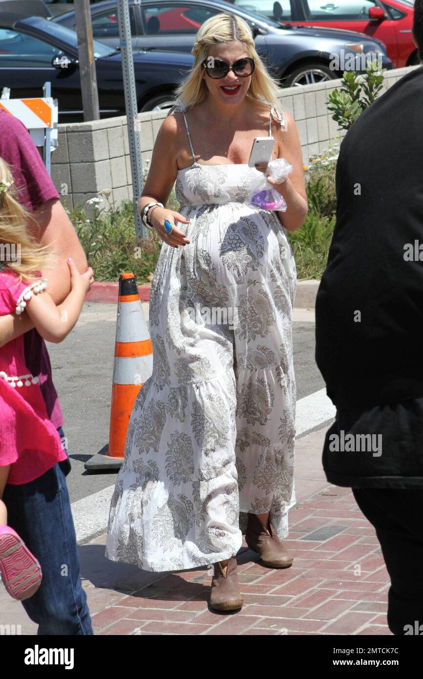 A heavily pregnant Tori Spelling in a long lose fitting white dress and