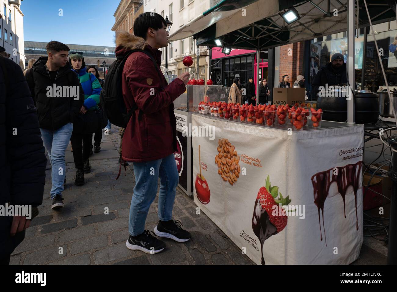 London - 02 27 2022: chocolate strawberry and candy apple vendor on James Street in Covent Garden with customer Stock Photo