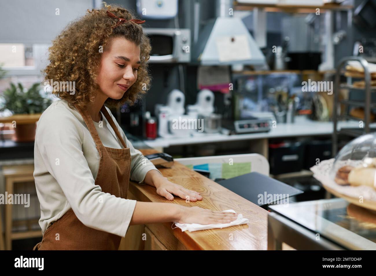 Positive bakery worker wiping counter with disinfecting spray Stock Photo