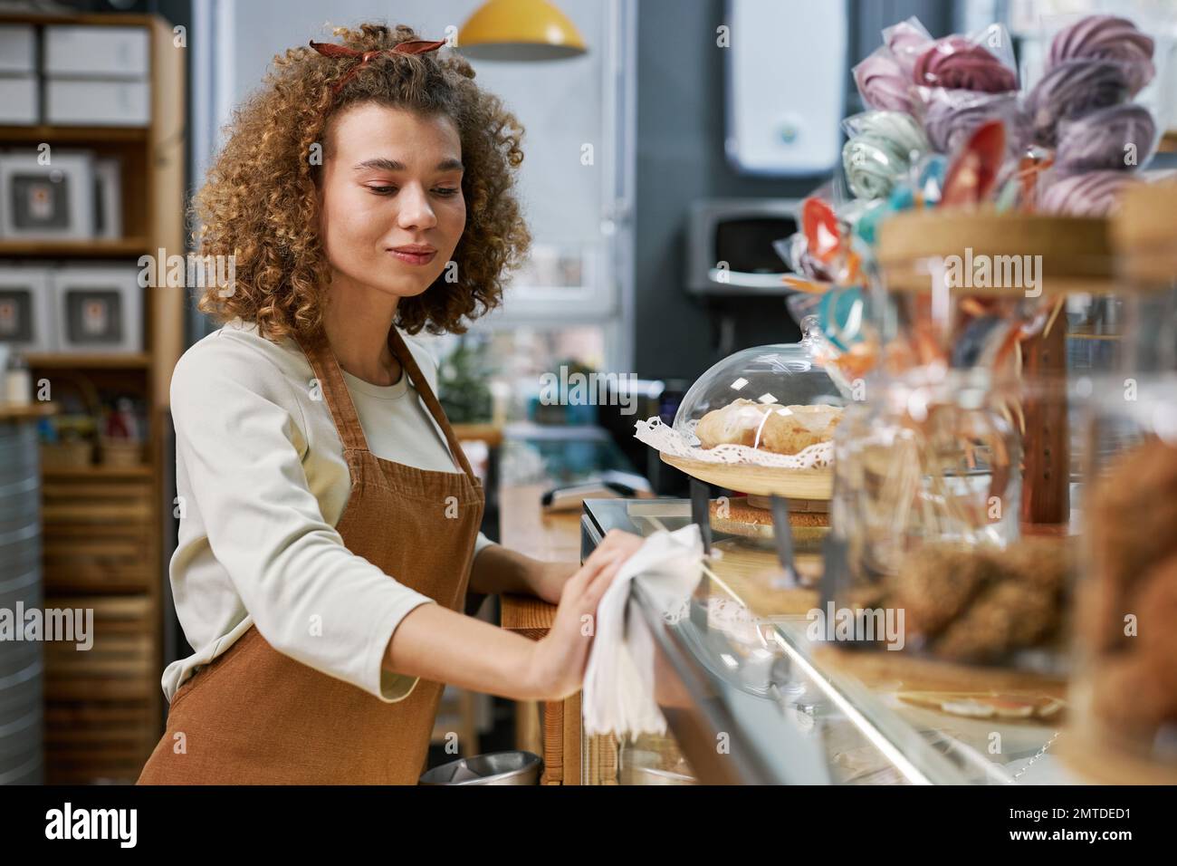 Smiling small bakery owner cleaning counter with disinfectant and soft cloth before opening Stock Photo