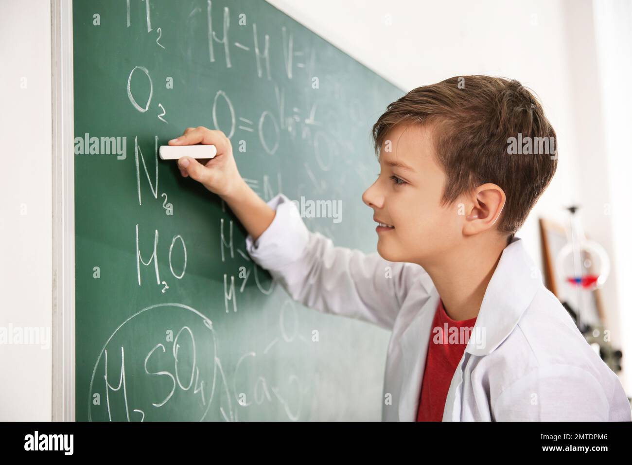Schoolboy writing chemical formulas on chalkboard in classroom Stock