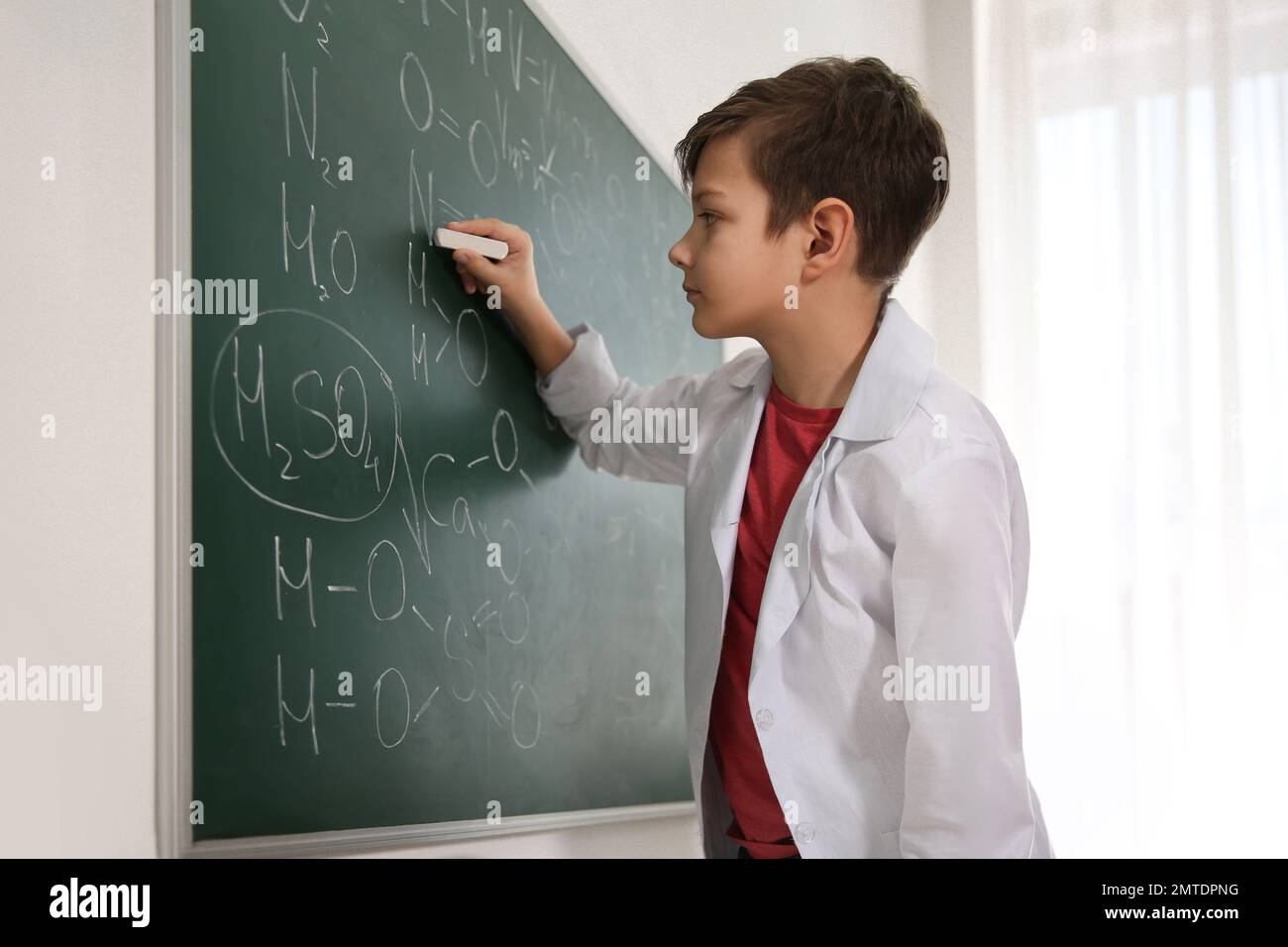 Schoolboy writing chemical formulas on chalkboard in classroom Stock