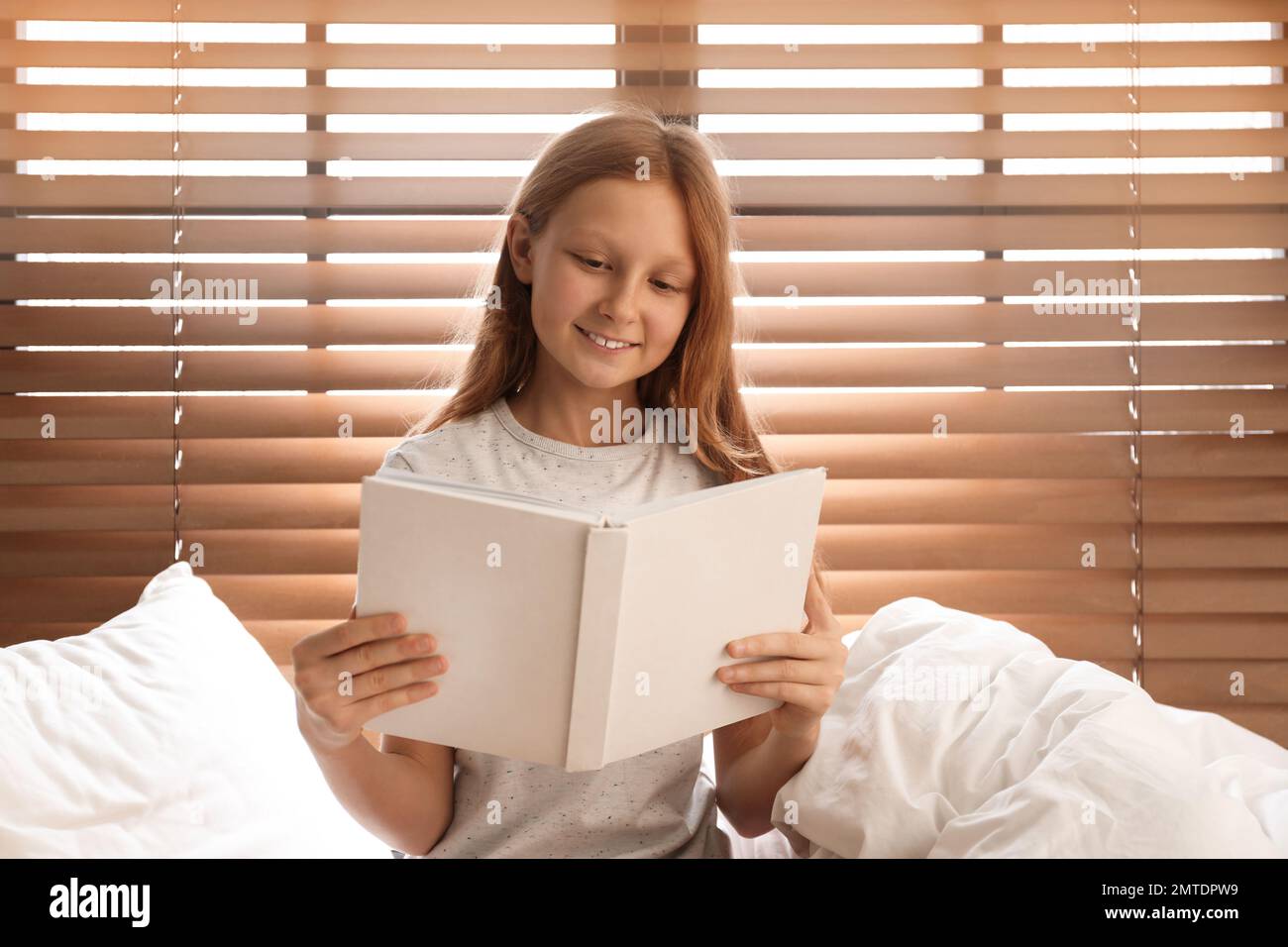 Cute preteen girl reading book on bed near window Stock Photo - Alamy