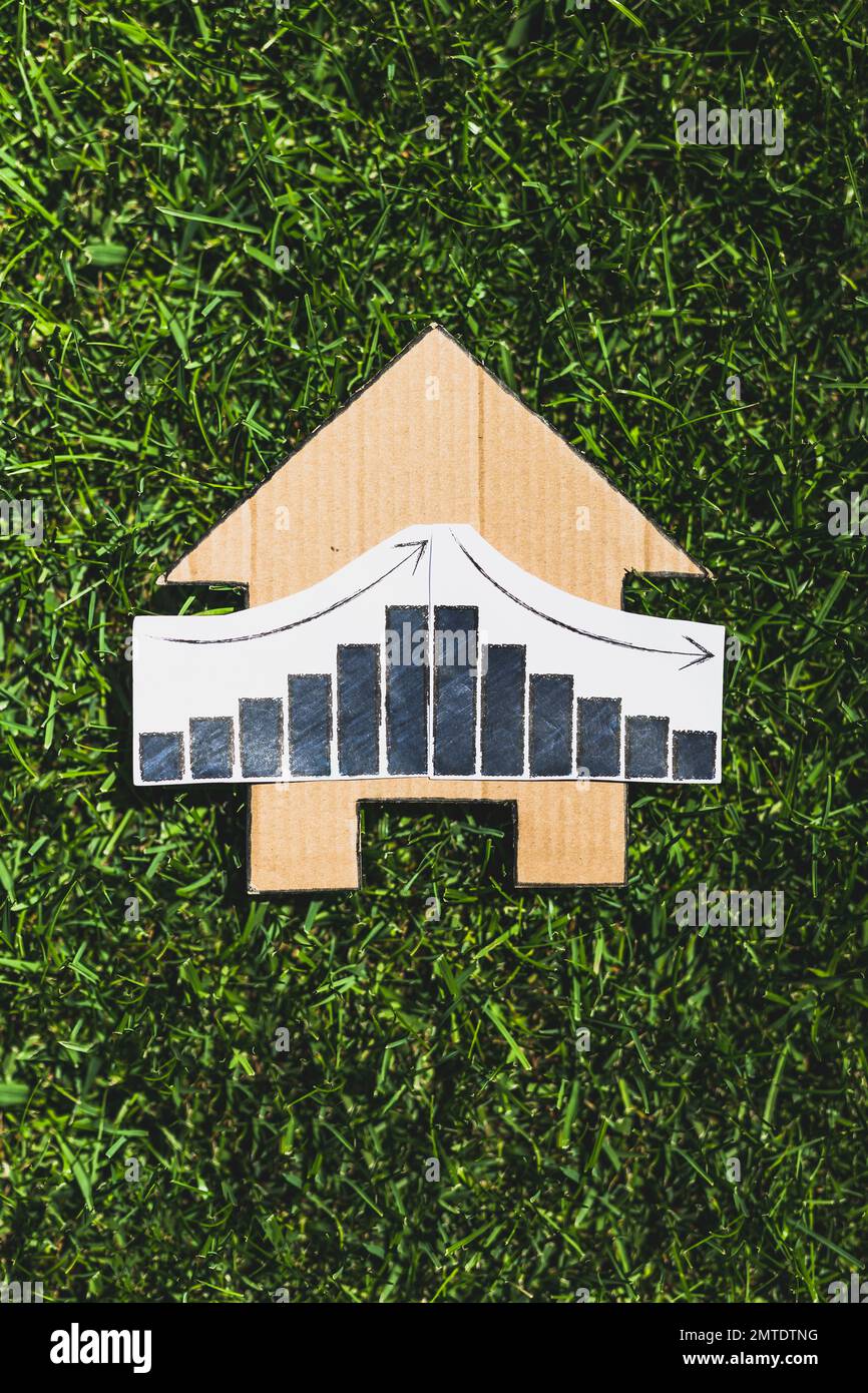 interest rates going up then down again, graph showing stats increasing and decreasing over house icon made of cardboard on green lawn Stock Photo