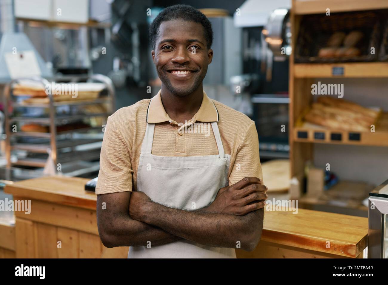 Portrait of happy baker in apron standing with arms crossed and smiling at camera Stock Photo