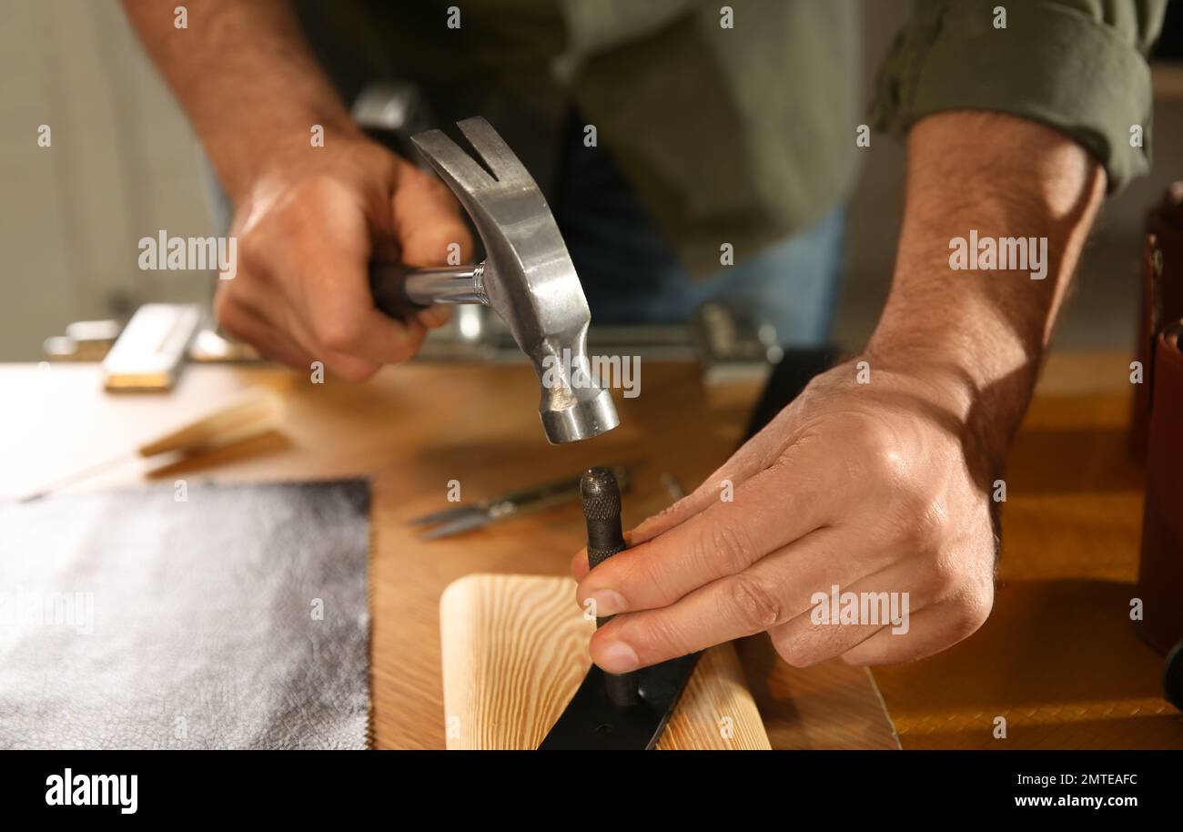 Man making holes in leather belt with punch and hammer at