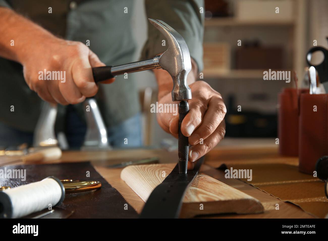 Man making holes in leather belt with punch and hammer at