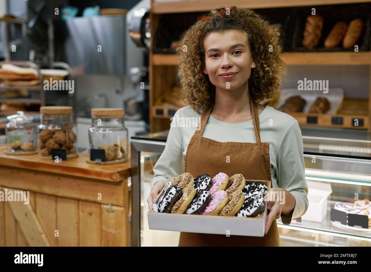 Positive baker holding box of delicious glazed donuts of different colors Stock Photo
