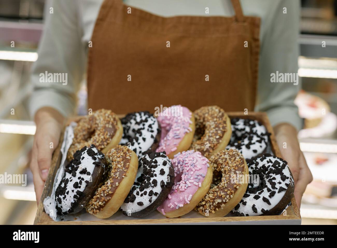 Tray with various fresh delicious donuts in hands of bakery owner Stock Photo