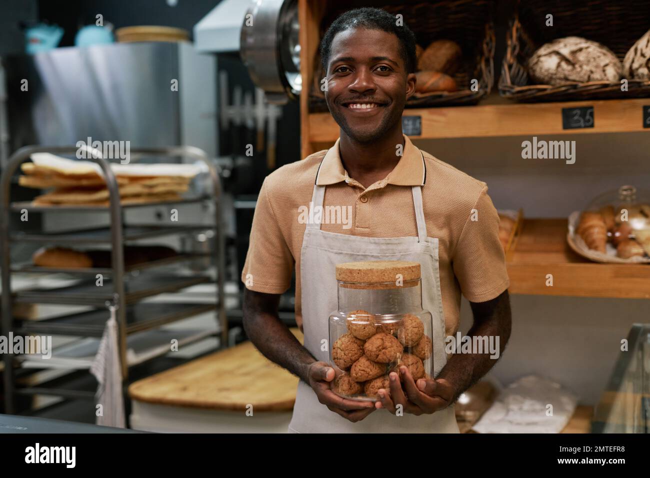 Portrait of smiling bakery worker holding glass jar of oatmeal cookies Stock Photo